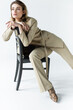 © LIGHTFIELD STUDIOS - stylish woman in beige suit posing on wooden chair on white