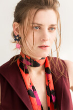 Portrait Of A Woman With Brown Hair In A Burgundy Vest With A Colored Headscarf And Bright Earrings Portrait Of A Woman With Brown Hair In A Burgundy Vest With A Colored Headscarf And Bright Earrings