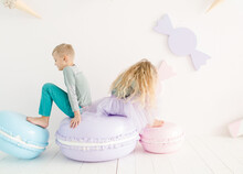 Boy And Girl In A Bright Colored Clothing In The Children's Room With Large Macaroon. Ice Cream And Macaroon