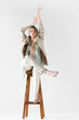 © LIGHTFIELD STUDIOS - trendy woman in suit sitting on wooden stool with hands above head on white