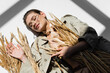 © LIGHTFIELD STUDIOS - top view of pleased woman in glasses, trench coat and scarf lying near wheat on white