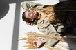 © LIGHTFIELD STUDIOS - high angle view of cheerful woman in glasses, trench coat and scarf lying near wheat on white