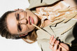 © LIGHTFIELD STUDIOS - top of model in glasses, trench coat and scarf lying and biting wheat spikelet on white