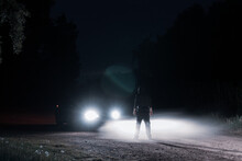 A Mysterious Hooded Figure Standing In Front Of A Car At Night