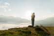 © Olga Sibirskaya/Stocksy - Woman standing with a dog on a meadow among mountains above clouds
