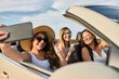 © Dangubic/Westend61 - Friends taking selfie on smart phone while enjoying road trip sitting in luxury car