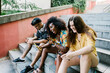 © Xavier Lorenzo/Westend61 - Young woman taking selfie while friends text messaging on smart phone sitting on steps