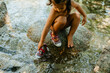 © VALENTINA BARRETO STUDIO/Westend61 - Cute girl playing in flowing water while sitting on rock during summer