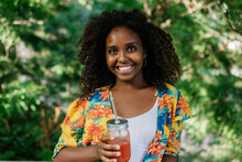 Smiling Young Woman Holding Juice While Standing In Park