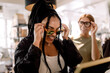© Maskot - Smiling female friends trying eyewear while talking at fashion store