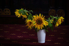 Sunflowers In Vase Standing On Dark Red Carpet With Ornament