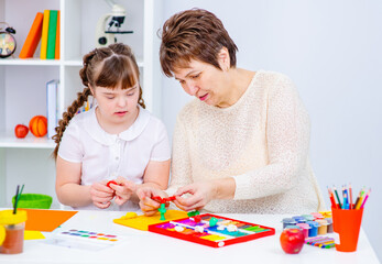 Wall Mural - The teacher shows the student with down syndrome how to do creativity. Girl with down syndrome smiles at teacher