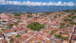 Aerial view panorama of historic town Barichara, Colombia situated on a cliff edge with white cloud covered mountain ridge in background

