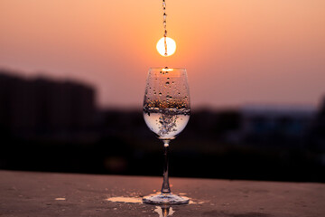 Clear liquid being poured into a wine glass at sunset