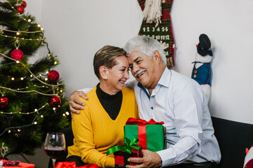 Wall Mural - Hispanic mature couple expressing love and enjoying Christmas together on a family Christmas celebration