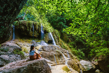 Woman relaxing on stone with waterfall at erawan national park in thailand.