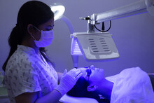 Young Woman Having Blue LED Light Facial Therapy Treatment In Beauty Salon. Beautician Wearing Face Mask Maintaining Safety Procedures During Appointment. Beauty, New Normal And Wellness