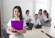 © Space_Cat - Young asian female nurse, student or practitioner standing in front of medical team holding clipboard looking at camera and smiling. Group of people behind discussing and interacting with each other