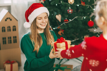 Two happy and cheerful sisters in trendy New Year's outfits give each other gifts at home under the tree. Christmas mood. Concept for New Years holiday at home.