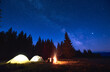 © anatoliy_gleb - Evening camping with campfire. People having a rest near tent city, enjoying valley of mountains in pine forest. Dark blue night sky is strewn with bright stars and Milky Way is visible on it.