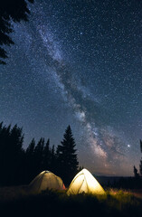 tourist camp in forest, warm summer night. two illuminated tents under breathtaking night sky full o
