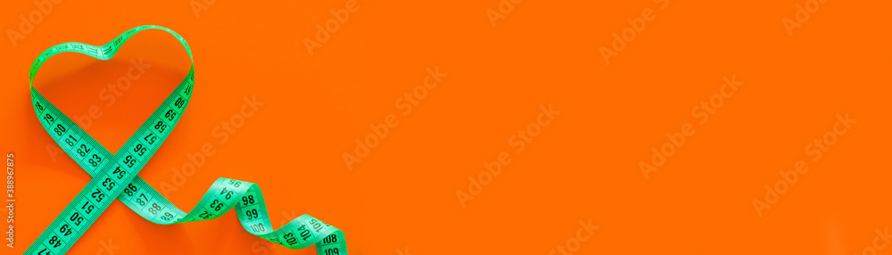 Green metric measuring tape on horizontal orange background. Mockup for body slimming, weight loss - obrazy, fototapety, plakaty 