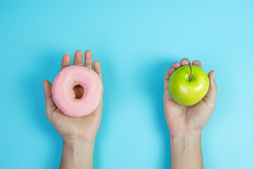 woman holding green apple and pink donut, female choose between fruit is Healthy food and sweet is unhealthy junk foods. Dieting, obesity, eating lifestyle and nutrition concept