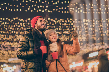 Wall Mural - Photo of two people students friends hold eggnog beverage mug girl point finger evening x-mas outdoors lights