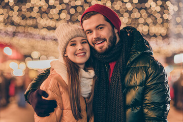 Poster - Photo of positive couple man hug his beloved boyfriend under x-mas tradition evening illumination outside wear season outerwear