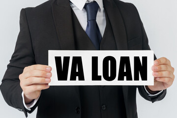 A businessman holds a sign in his hands which says VA LOAN