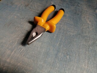 New metal pliers with yellow handles on a gray wooden surface
