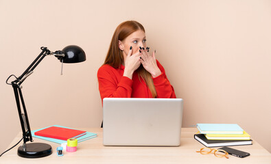 Young student woman in a workplace with a laptop covering mouth and looking to the side