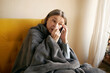 © shurkin_son - Tired sick senior woman having cold, blowing nose in tissue, sitting on couch with mobile, calling doctor or relative, suffering from headache, fever or high temperature. Technology, age and health