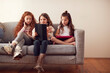 © Monkey Business - Group Of Girls With Friends Sitting On Sofa At Home Playing On Digital Tablet And Mobile Phones