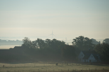Wall Mural - Landscape of foggy morning in Skåne (Scania) showing flat farmlands and wind turbine generating renewable energy