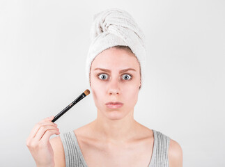 Closeup portrait of a woman applying dry cosmetic tonal foundation on the face using makeup brush.