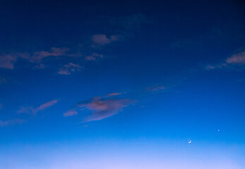 Wall Mural - blue sky at twilight with sparse pink clouds and crescent moon rising
