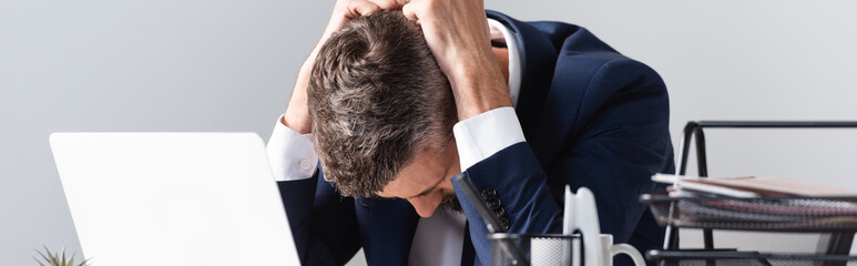 Tired businessman sitting near laptop and papers on blurred foreground in office, banner