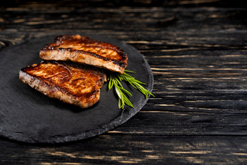 Wall Mural - juicy piece of fried meat lies on a stone plate against a black wooden table