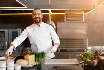 handsome young african chef standing in professional kitchen in restaurant preparing a meal of meat 