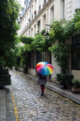 Wall Mural - Portrait on back view of woman walking in the cobbelstone street with a rainbow umbrella