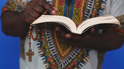Wall Mural - Unrecognizable African black man in traditional dress with rosary reading the Holy Bible . High quality photo