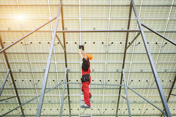 Wall Mural - Installing and wiring of solar photo voltaic panel. Worker in orange uniform connects solar panels at the station. Ecology power conservation concept.