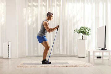 Sticker - Guy exercising with a resistance band at home while watching tv