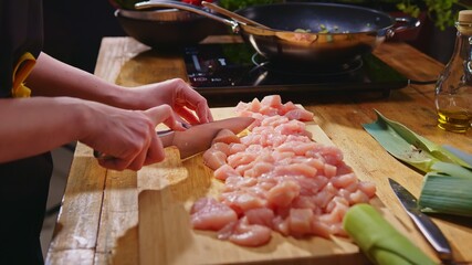 Wall Mural - Woman slicing meat for cooking on kitchen table. Closeup hands. Cosy dark room. Real, authentic cooking.