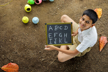 Indian child writing A B C D alphabet on Chalkboard