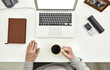 © Svitlana - Top view of aged male employee senior intern holding a cup of coffee while sitting at desk in modern office, Notebook, picture frame, cell phone, glasses and laptop on the table