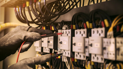 Close-up hand of electrical engineer using measuring equipment to checking electric current voltage at circuit breaker and cable wiring system for maintenance in main power distribution board.