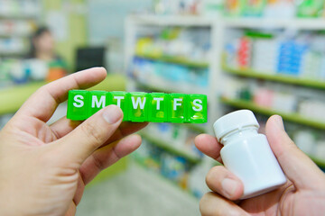 Wall Mural - Hand holding pill box and medicine bottle on pharmacy store background.