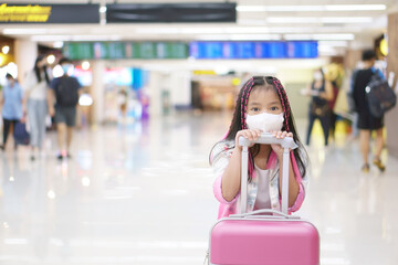 Asian child or kid girl wearing white face mask to protect coronavirus or PM 2.5 dust with dragging luggage or baggage and pink suitcase in airport for holiday travel to happy on summer vacation trip